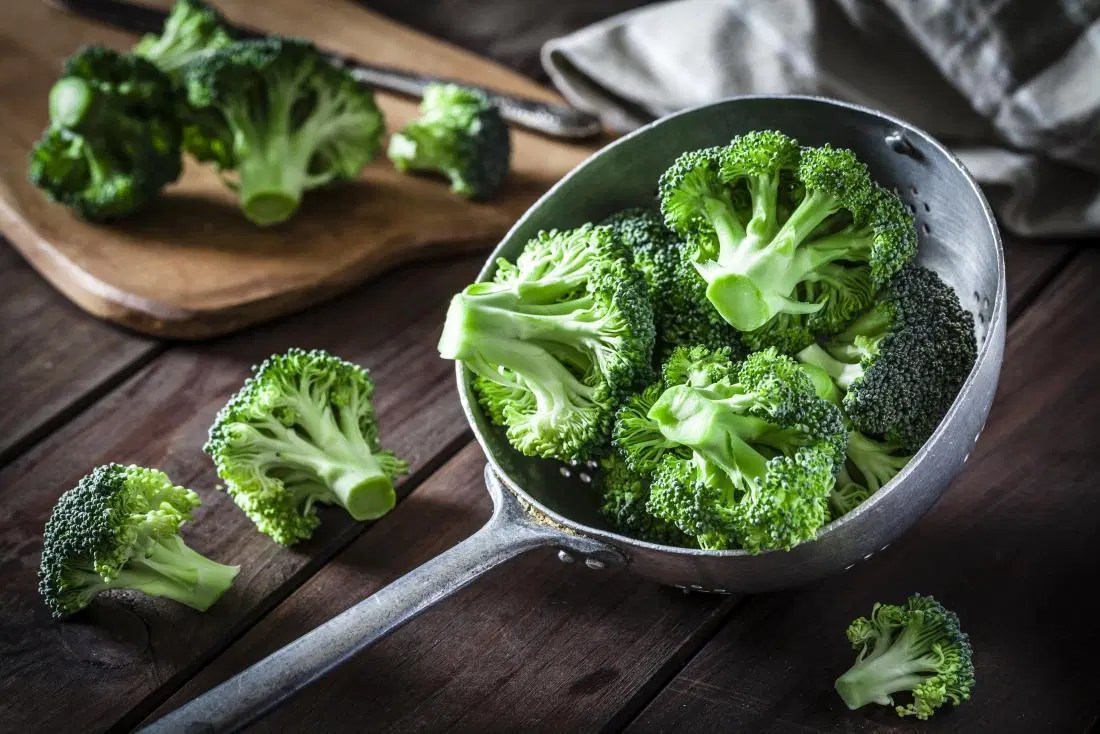 Broccoli in spoon on wooden table.