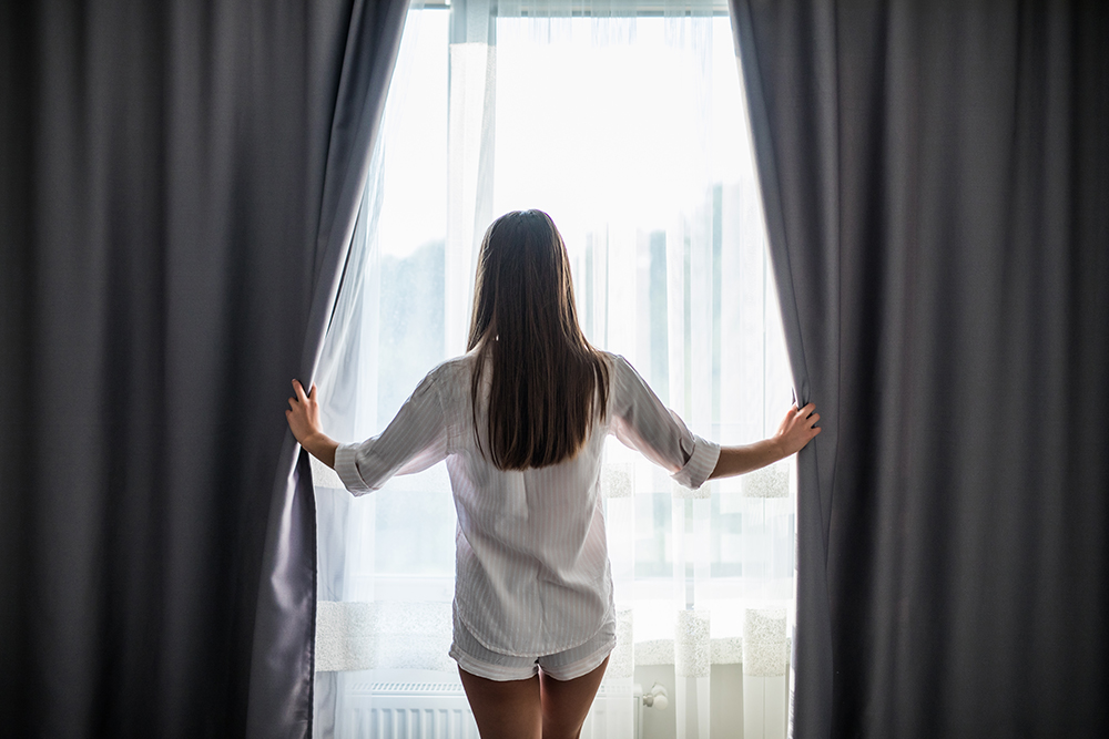 beautiful-young-woman-opening-curtains-looking-through-window.jpg