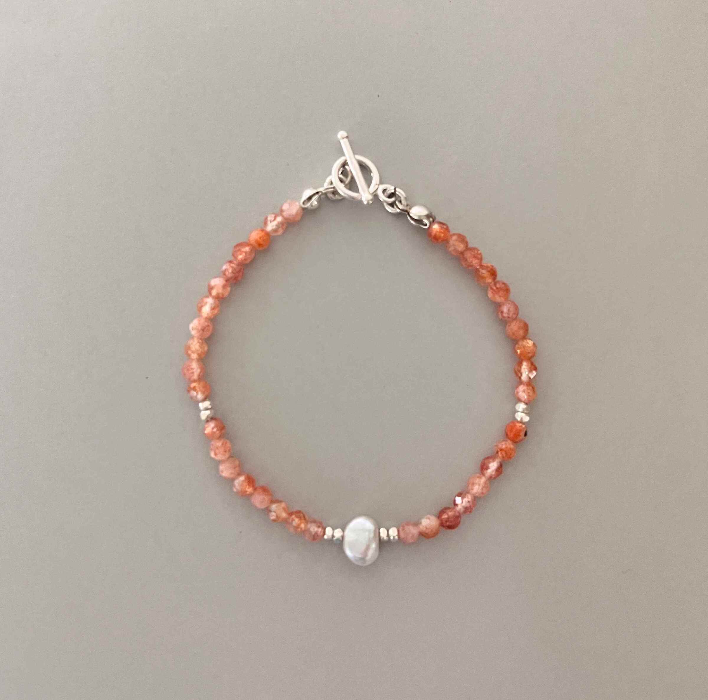 Solène 太陽石手鍊以閃耀橘光的鑽切太陽石點綴卡倫銀珠，中央一顆不規則巴洛克珍珠.