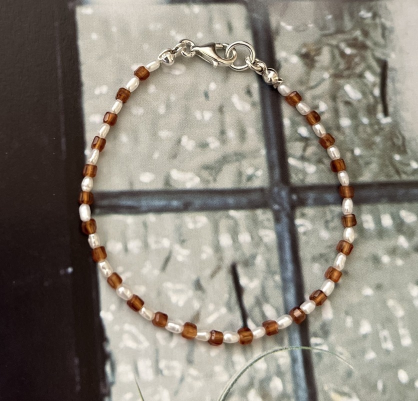 由紅棕色的石榴石珠和潔白淡水珍珠串成的細緻手鍊，搭配銀色扣環，帶有優雅的風格。