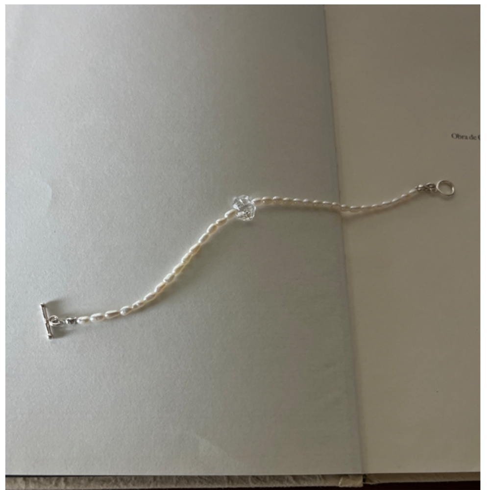 Matilda & Co.的 Luna Blanche 天然米粒珍珠與赫基蒙水晶手鍊，搭配銀色 OT 扣，靜置於翻開的書頁上。