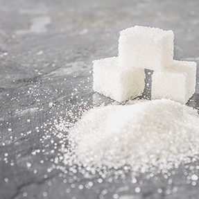 Food. Cubes of sugar and sugar sand on a dark gray background.