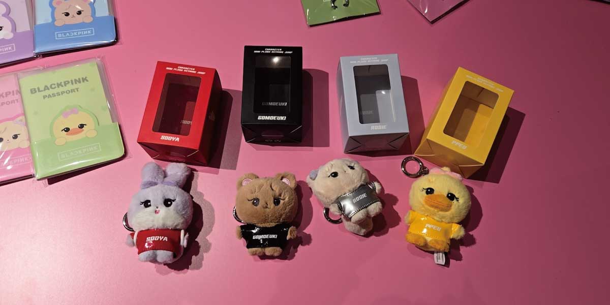 BLACKPINK 成員角色吊飾與彩色護照夾擺拍,粉紅桌面背景。