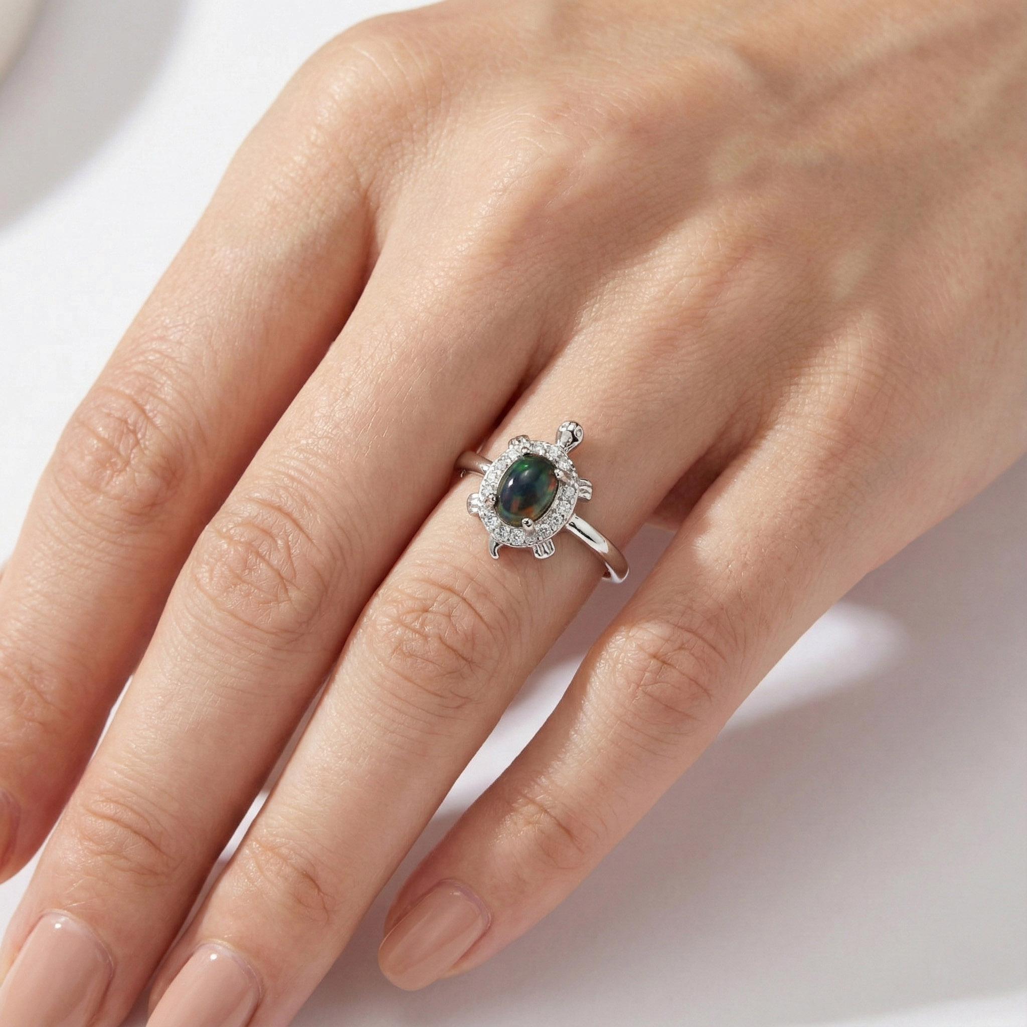 歐泊彩石海龜戒指實際配戴於手指上,橢圓歐泊呈現低調藍綠變彩,銀色海龜造型小巧精緻,展現日常佩戴的真實比例與優雅質感