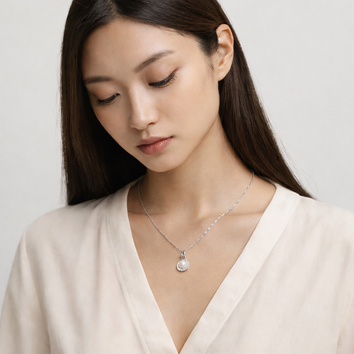 真人女性配戴簡約天然小珍珠純銀項鍊，珍珠貝殼墜飾自然落在鎖骨中央，搭配米白色襯衫的日常穿搭情境