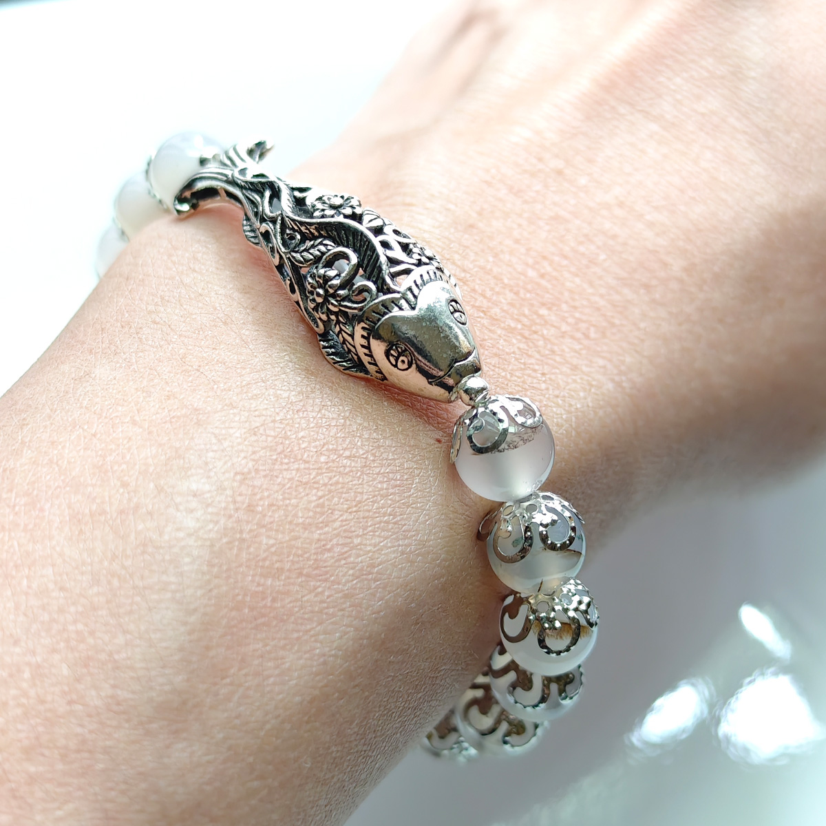 銀色雕刻鯉魚白玉髓水晶手鍊實際配戴於手腕,窗邊自然光下呈現溫潤質感與細節