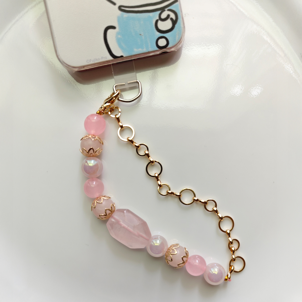 晶手機掛繩細節展示,柔和粉色水晶與金色鍊條結合,適合日常隨身配戴的人緣系手機吊飾