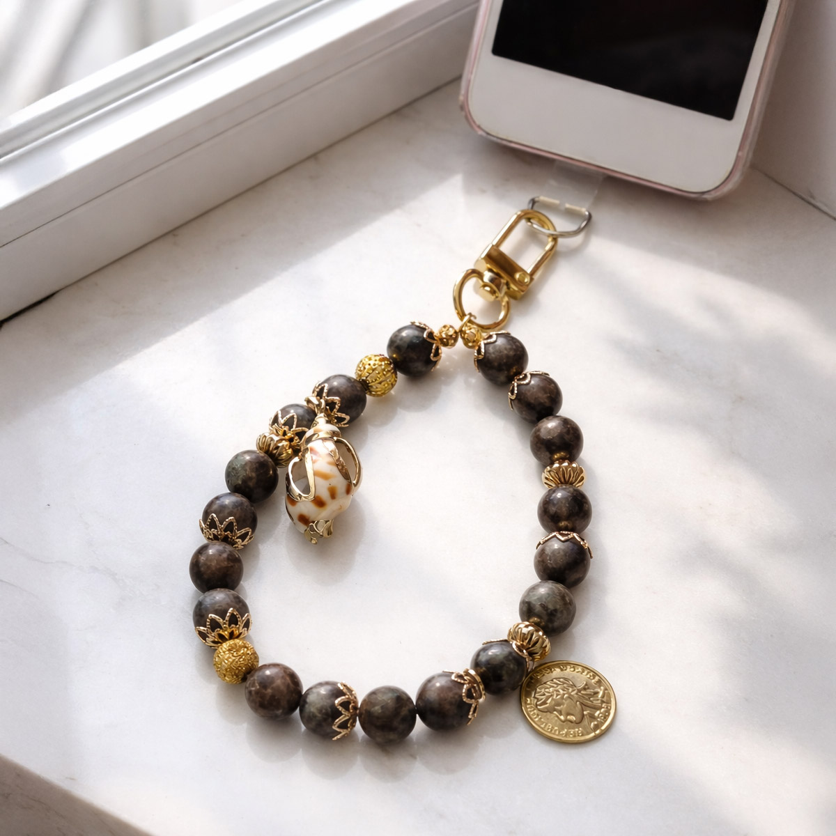 靜穩彼得石守護手機掛繩連接手機使用情境，窗邊自然光呈現彼得石紋理與金色吊飾細節