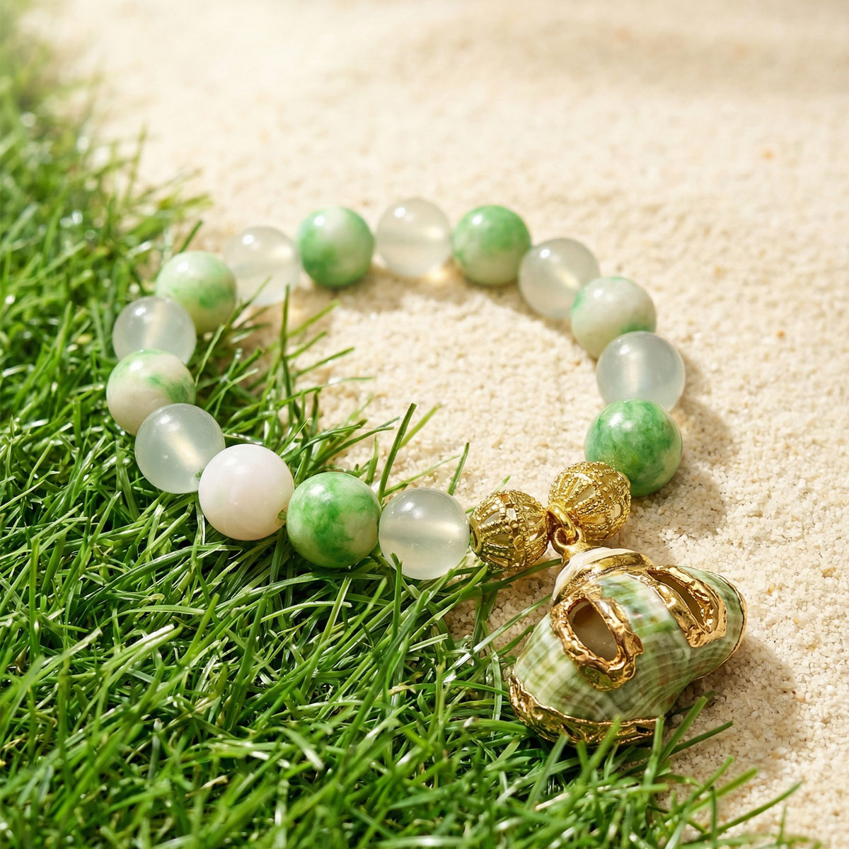 翡翠綠玉髓金貝殼手鍊置於草地與細沙間,自然光下呈現清新綠白玉髓色澤與金色貝殼吊飾,展現貼近日常的療癒氛圍