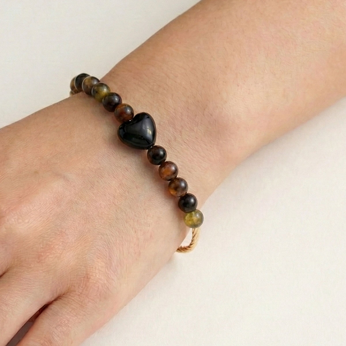 black-obsidian-heart-black-tourmaline-bracelet-worn黑曜石愛心黑碧璽手鍊配戴於左手腕,深色系水晶搭配金色扭紋管,呈現低調沉穩的日常風格
