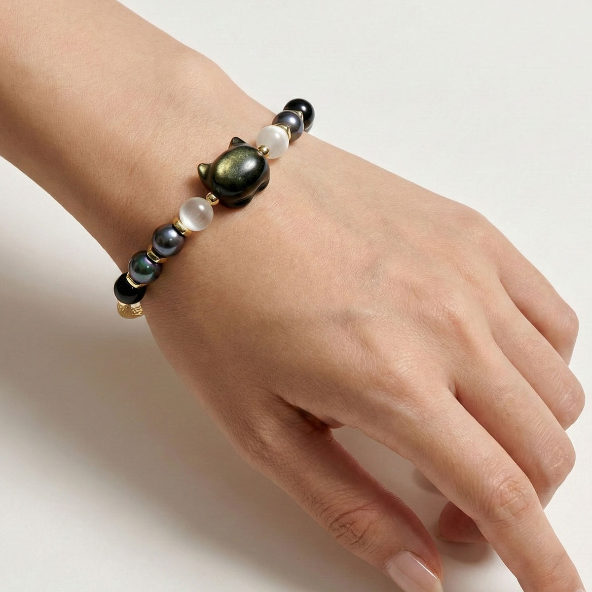 金曜石萌貓黑珍珠手鍊手腕近拍，貓形金曜石主珠搭配黑珍珠與白色水晶，呈現細緻配戴質感