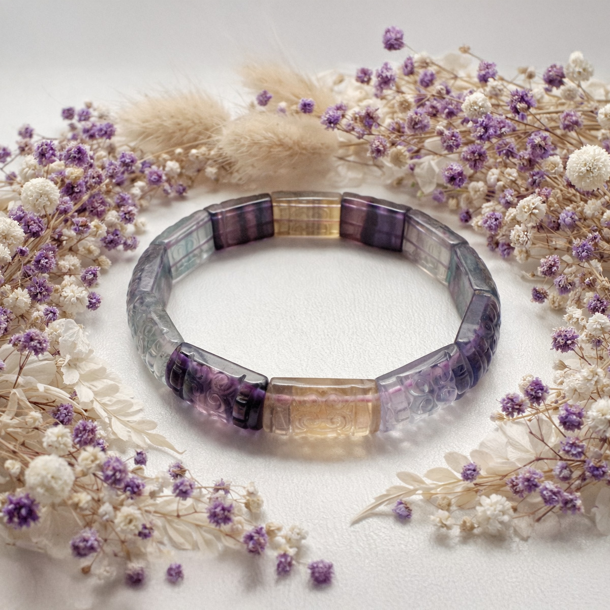 彩虹螢石雕刻回紋手排,搭配紫白色滿天星花圈的自然風格靜物情境照