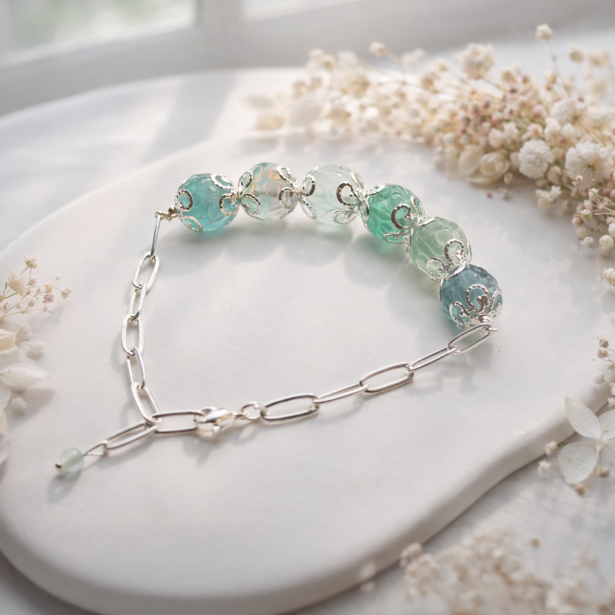 恬靜綠瑩石手鍊置於窗邊自然光下，淡綠色瑩石與白色花材襯托出溫柔安定的日常佩戴氛圍