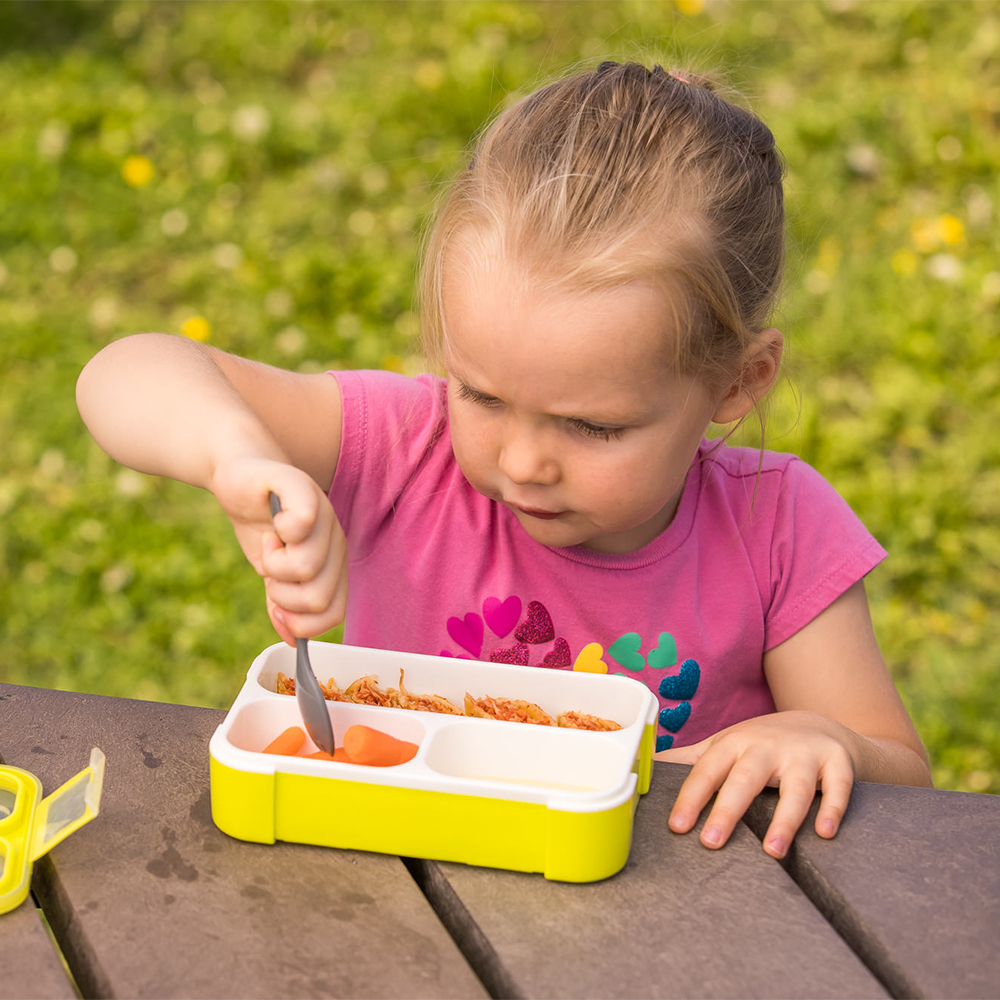 B0123L_-_Bento_-_Lifestyle_-_Girl_eating_from_opened_green_lunchbox_with_fork_-_Park_background_-_Landscape_Format